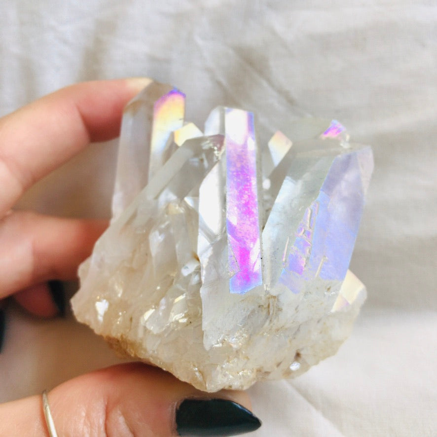 One-of-a-kind Angel Aura Quartz cluster held in hand, showing iridescent rainbow flashes across natural crystal points - Let's Jam crystal collection