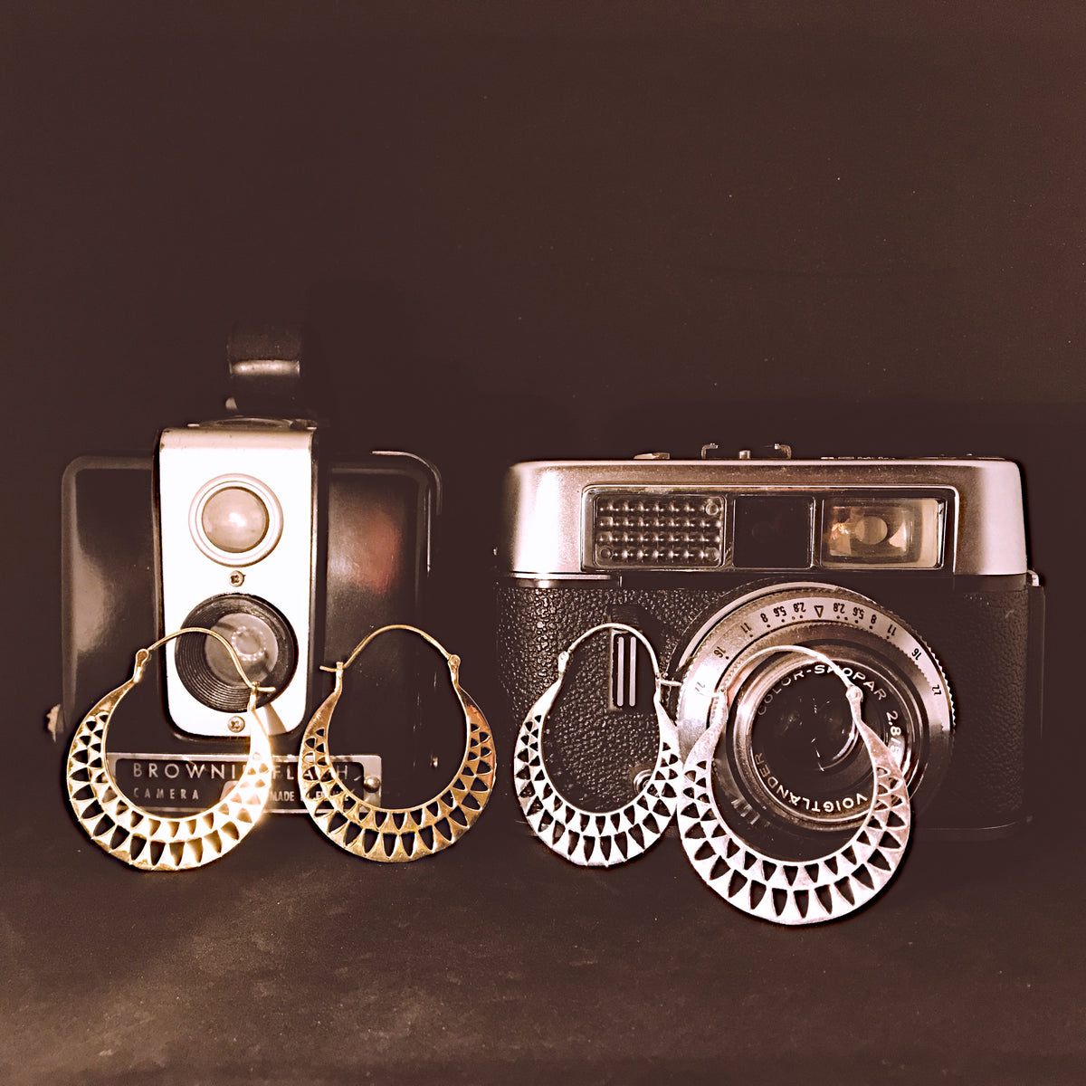 Gold and silver ethnic hoop earrings with a geometric mesh pattern, styled next to vintage cameras - Let's Jam jewellery collection