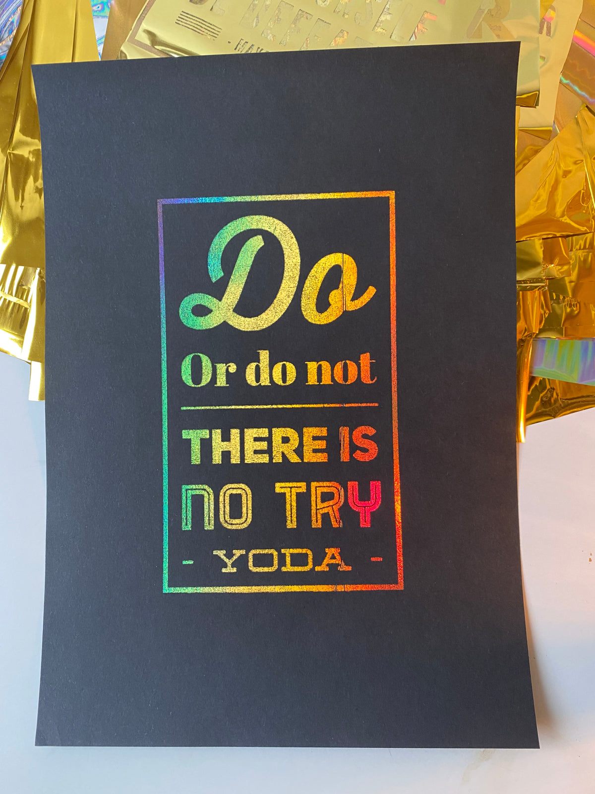 A black print with the Yoda quote "Do or do not, there is no try" in rainbow holographic lettering, displayed beside iridescent gift wrap - Let's Jam print collection