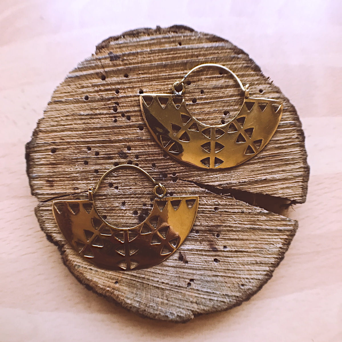 Gold brass earrings with a geometric Aztec-style triangle cut-out design, displayed on a wooden slice - Let's Jam jewellery collection
