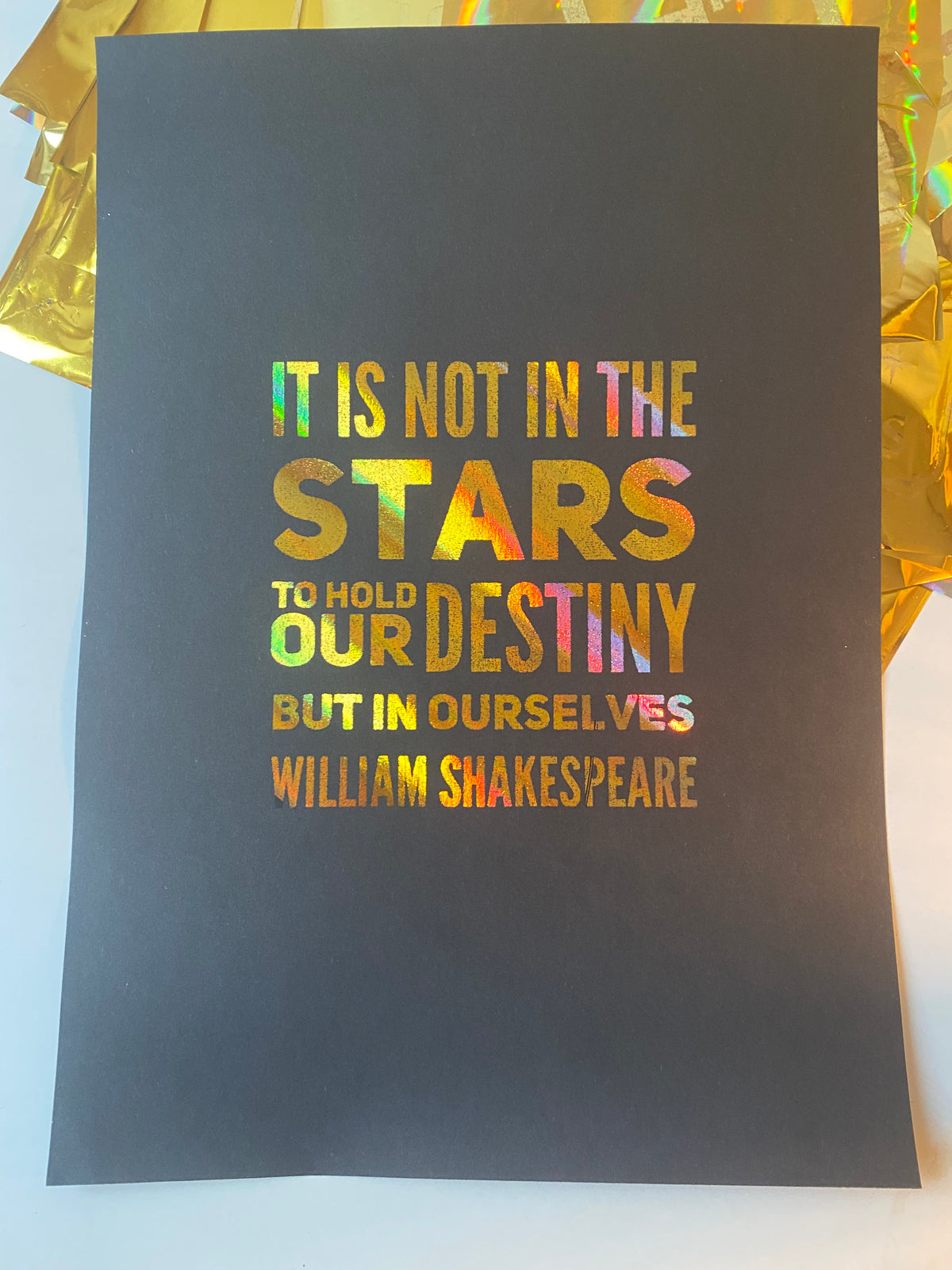 A black print with the William Shakespeare quote "It is not in the stars to hold our destiny but in ourselves" in rainbow holographic lettering, beside iridescent gift wrap - Let's Jam print collection