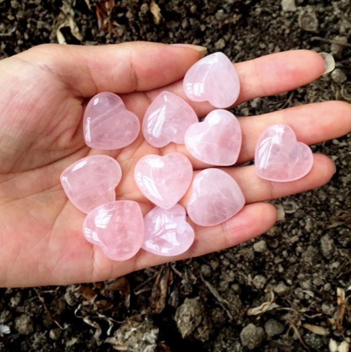 Handful of polished rose quartz heart-shaped crystals cupped in an open palm outdoors - Let's Jam crystal collection