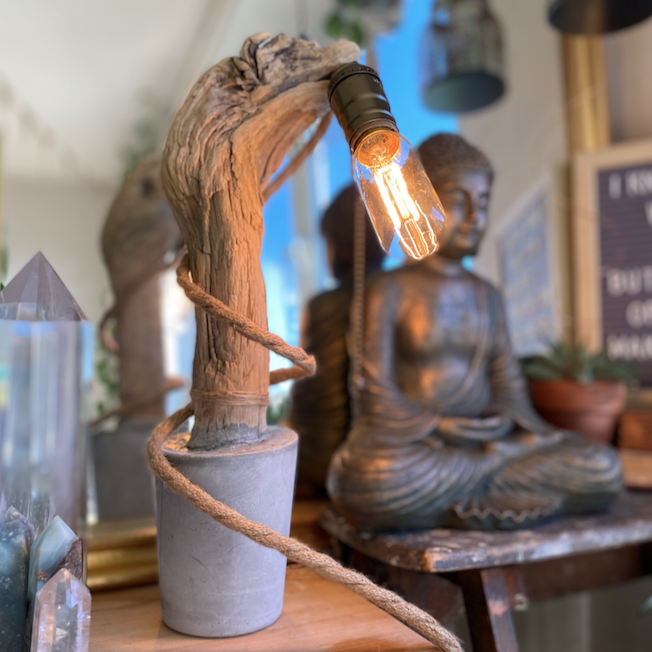 One-of-a-kind concrete lamp with a curved real wooden branch holding a glowing Edison-style bulb, displayed beside a bronze Buddha statue and quartz crystal points - Let's Jam collection