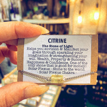 Load image into Gallery viewer, Handmade stainless steel bracelet with a natural citrine crystal charm, held alongside a printed card describing the stone's manifesting properties - Let's Jam jewellery collection
