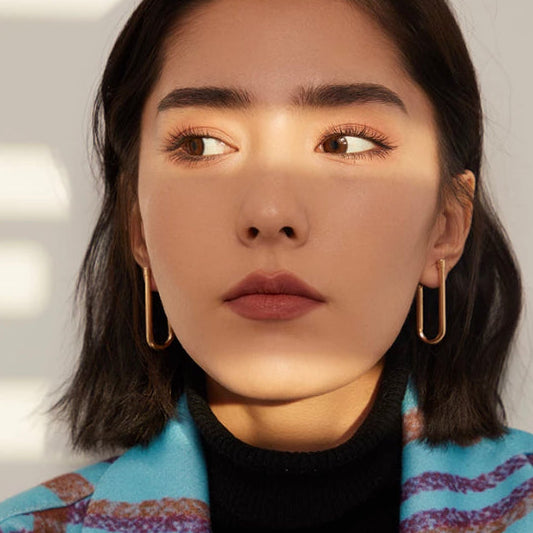 Model wearing gold-plated copper U-shaped drop earrings, styled with a colourful striped blazer - Let's Jam jewellery collection