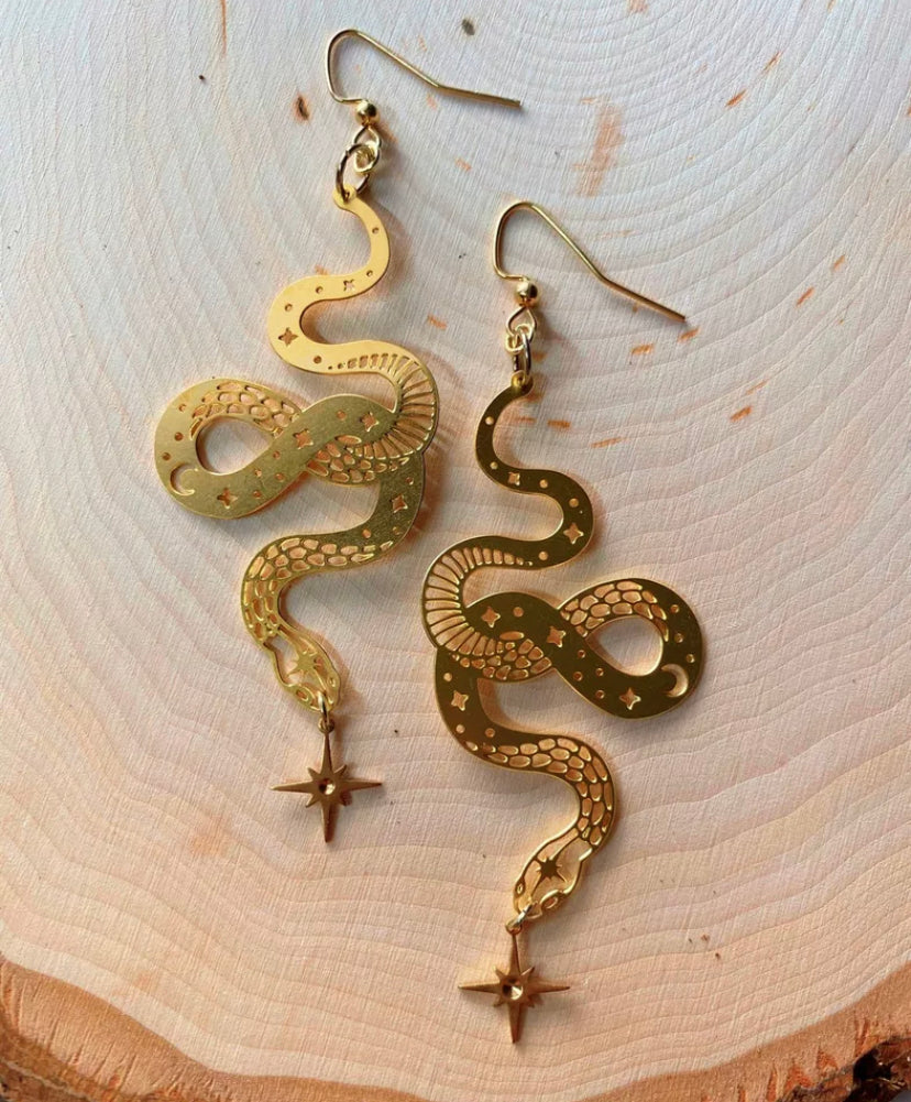 Gold-plated coiled snake drop earrings with a hanging star charm, laid on a pale wooden surface - Let's Jam jewellery collection