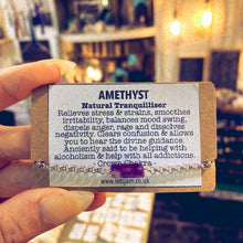 Load image into Gallery viewer, Handmade stainless steel bracelet with a natural amethyst crystal charm, held alongside a printed card describing the stone's calming properties - Let's Jam jewellery collection
