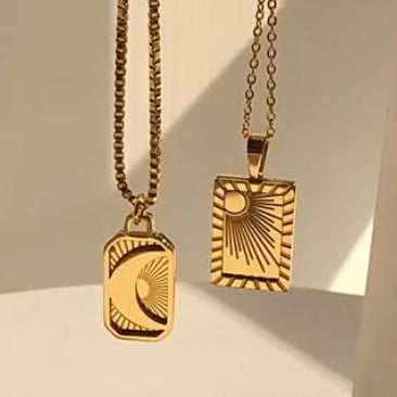 Gold-plated moon and sun pendant necklaces with textured sunburst and crescent moon charms, hung together against a sunlit architectural backdrop - Let's Jam jewellery collection