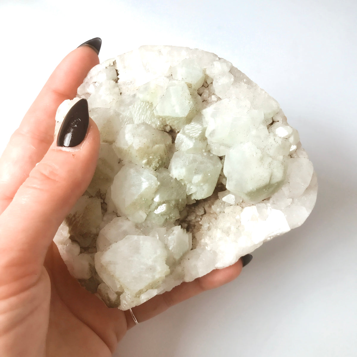 A hand holding a large raw milky quartz crystal cluster with jagged, layered white and pale green formations - Let's Jam crystal collection