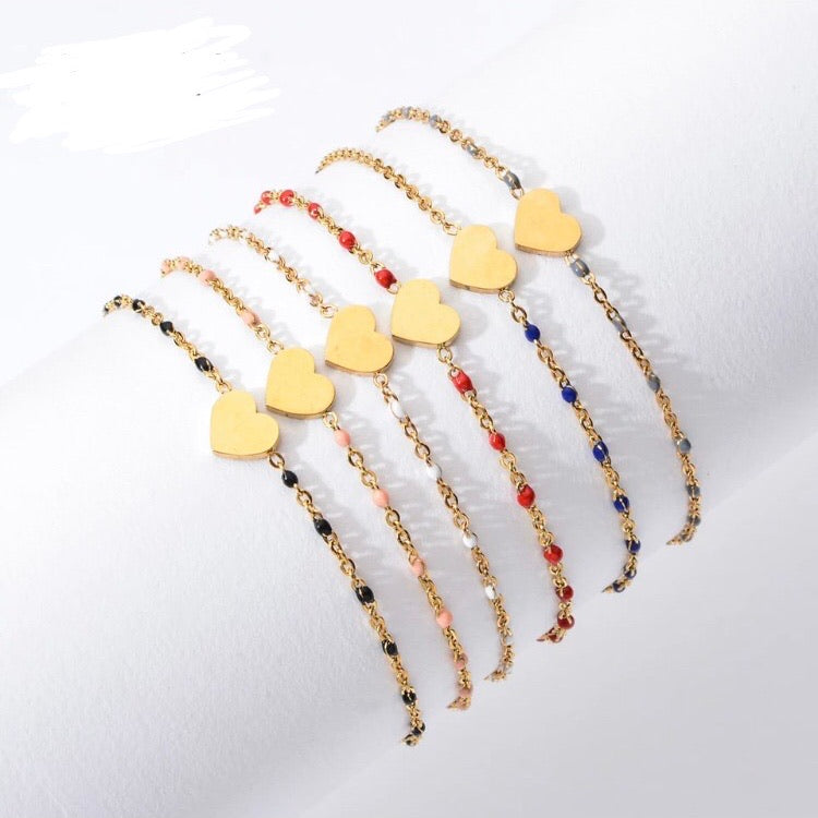 A row of gold-tone chain bracelets with yellow enamel heart charms and colourful beaded accents in red, pink, black and navy - Let's Jam jewellery collection