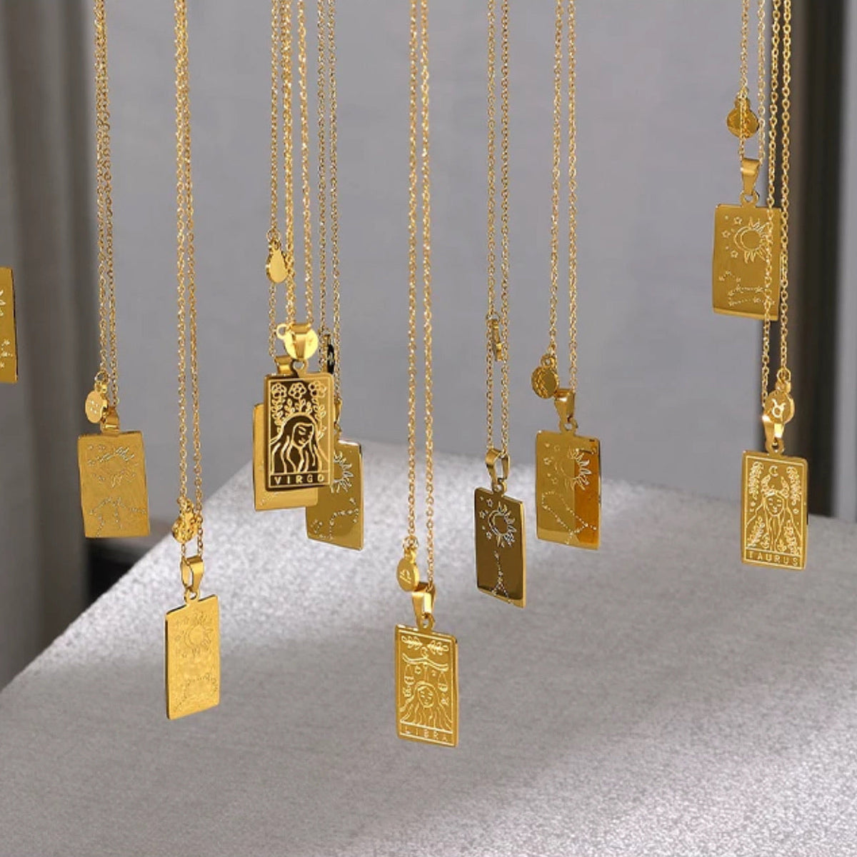 Gold-plated zodiac sign pendant necklaces engraved with individual constellation and horoscope designs, hung together against a neutral backdrop - Let's Jam jewellery collection